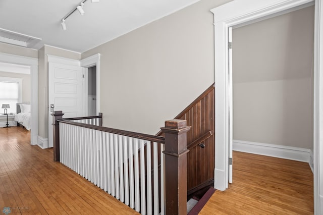 hallway featuring baseboards, hardwood / wood-style flooring, an upstairs landing, and attic access