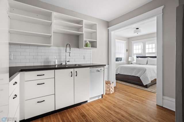 kitchen featuring open shelves, dark countertops, white dishwasher, a sink, and hardwood / wood-style floors