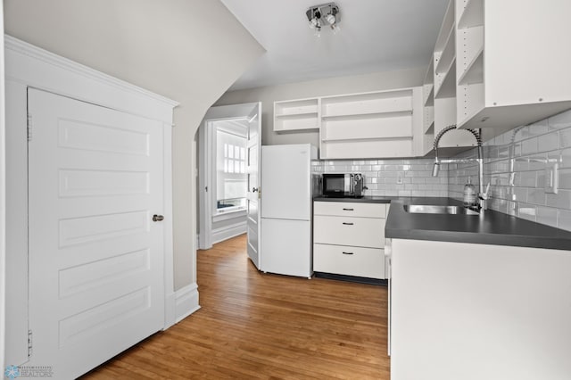 kitchen featuring open shelves, dark countertops, freestanding refrigerator, a sink, and wood finished floors