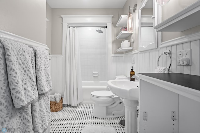 full bath with wainscoting, shower / bath combo with shower curtain, and toilet