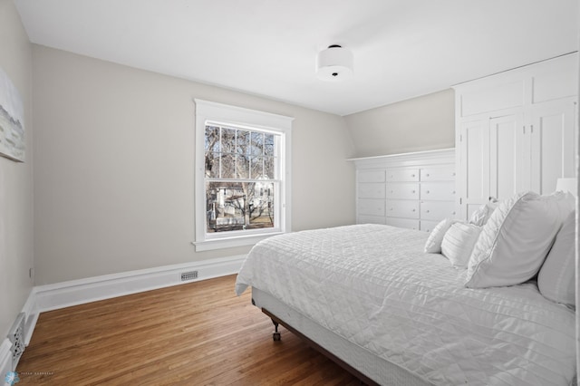 bedroom with visible vents, baseboards, wood finished floors, vaulted ceiling, and a closet