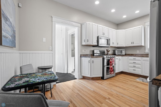 kitchen featuring dark countertops, light wood-style flooring, appliances with stainless steel finishes, and white cabinets