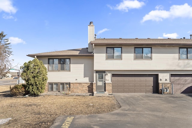 split level home with a garage, driveway, brick siding, and a chimney