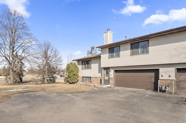 tri-level home with brick siding, driveway, and a chimney