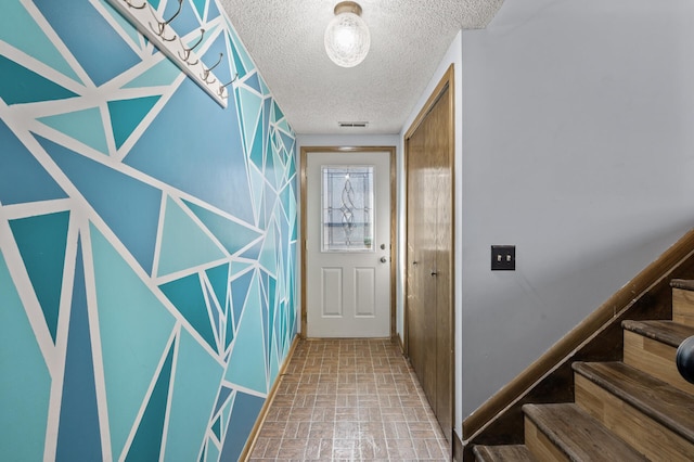 hallway featuring brick floor, visible vents, stairway, and a textured ceiling