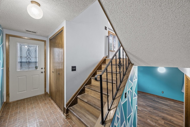 foyer featuring a textured ceiling, brick floor, visible vents, baseboards, and stairs