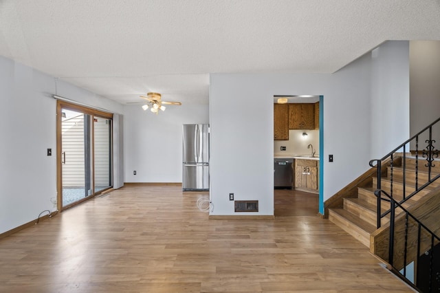 unfurnished living room with light wood-style flooring, stairs, visible vents, and a sink