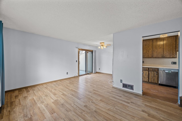 unfurnished living room with a textured ceiling, light wood-style flooring, visible vents, and baseboards