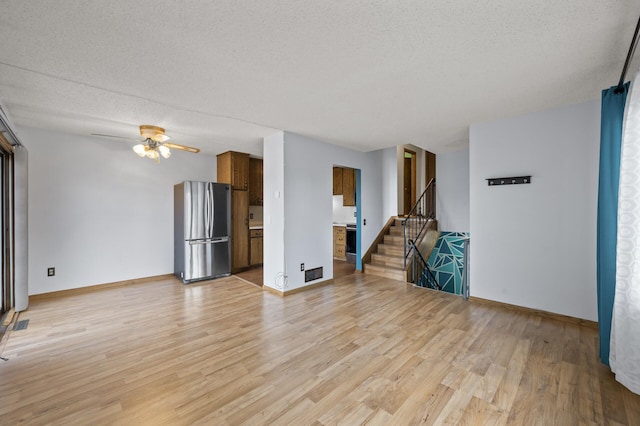 unfurnished living room featuring stairway, baseboards, light wood-style flooring, and a textured ceiling