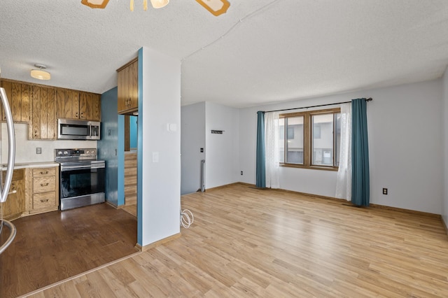 kitchen featuring a textured ceiling, wood finished floors, light countertops, appliances with stainless steel finishes, and brown cabinets