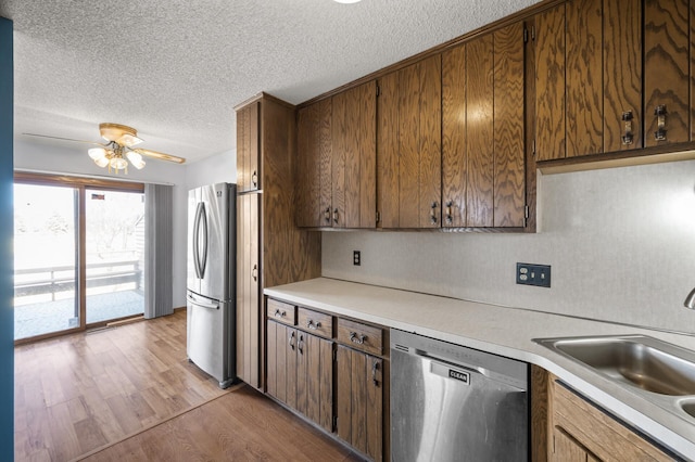 kitchen with appliances with stainless steel finishes, light countertops, a sink, and light wood-style flooring