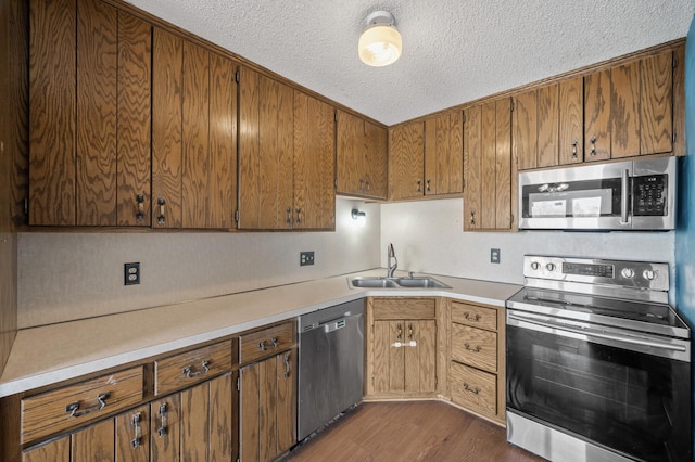 kitchen with dark wood-style flooring, stainless steel appliances, a sink, and light countertops