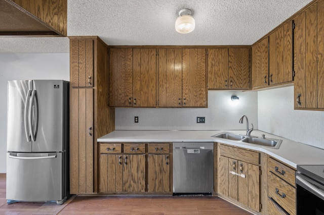 kitchen featuring appliances with stainless steel finishes, light countertops, a sink, and wood finished floors