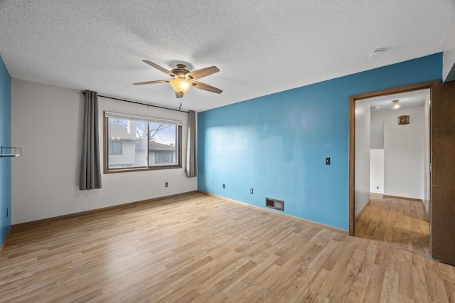 empty room featuring a textured ceiling, wood finished floors, visible vents, baseboards, and a ceiling fan