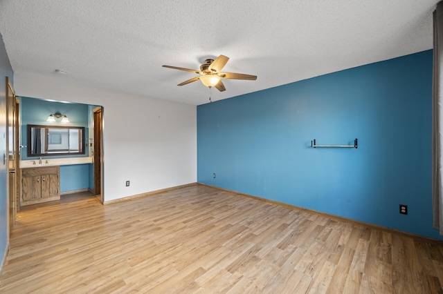 unfurnished living room featuring ceiling fan, a textured ceiling, a sink, baseboards, and light wood-style floors