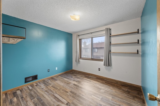 spare room with a textured ceiling, wood finished floors, visible vents, and baseboards