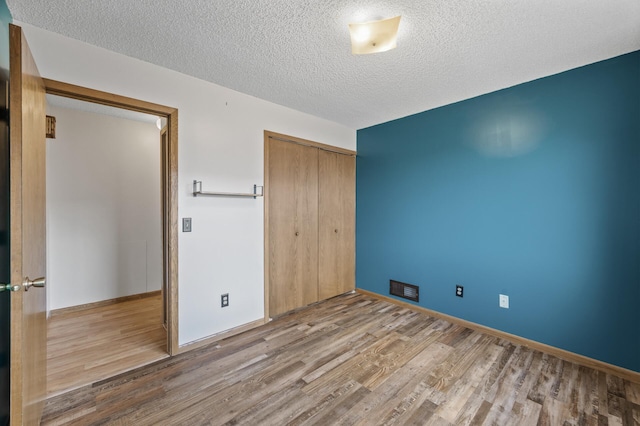 unfurnished bedroom featuring a textured ceiling, visible vents, a closet, and wood finished floors