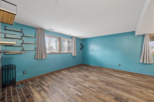 empty room featuring visible vents, a textured ceiling, baseboards, and wood finished floors