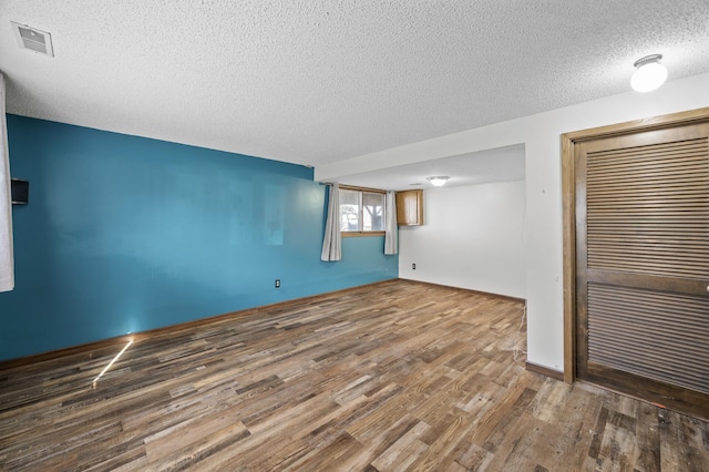 empty room with a textured ceiling, wood finished floors, and visible vents