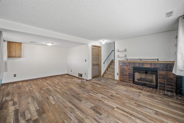 unfurnished living room featuring baseboards, stairway, wood finished floors, a textured ceiling, and a fireplace