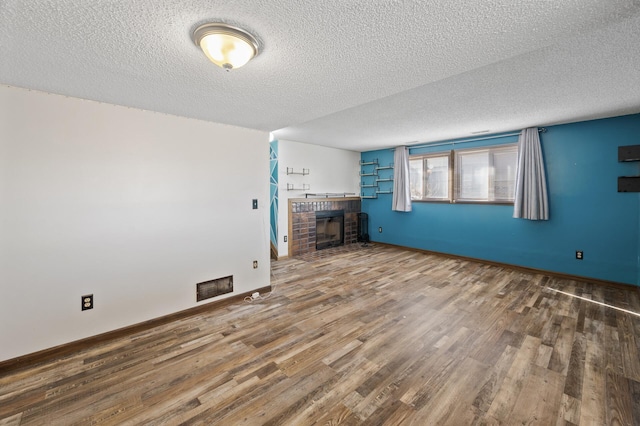 unfurnished living room featuring a textured ceiling, a fireplace, wood finished floors, visible vents, and baseboards