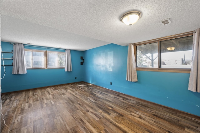 empty room featuring visible vents, a textured ceiling, baseboards, and wood finished floors