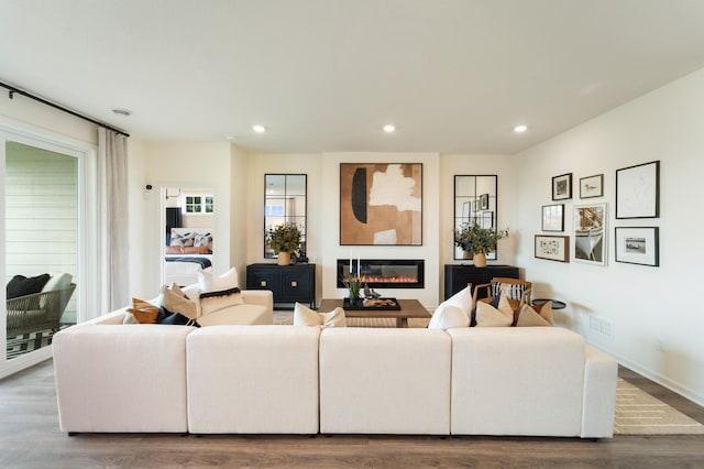 living room featuring recessed lighting, visible vents, a glass covered fireplace, wood finished floors, and baseboards