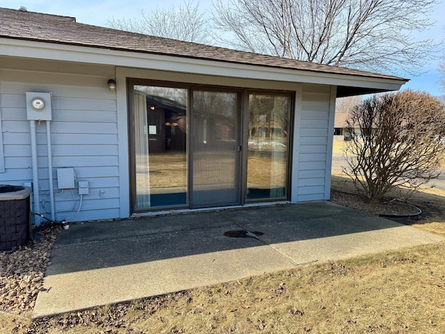 entrance to property featuring a shingled roof and cooling unit