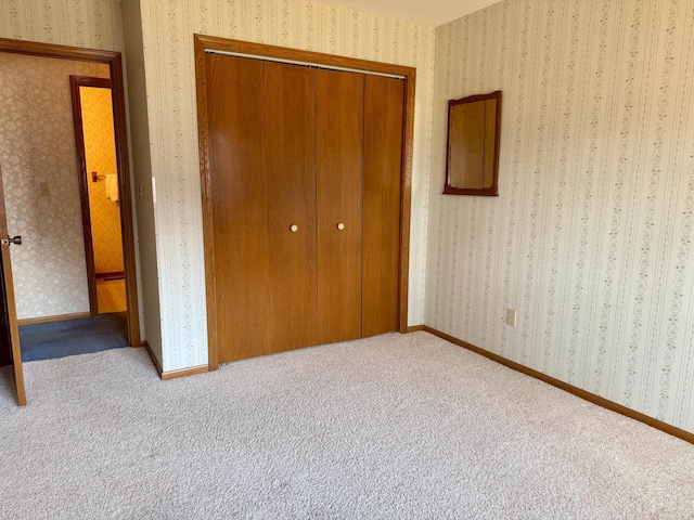 unfurnished bedroom featuring carpet floors, a closet, baseboards, and wallpapered walls