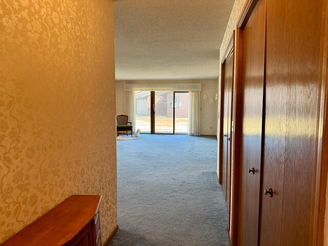 corridor with a textured ceiling, carpet flooring, and wallpapered walls