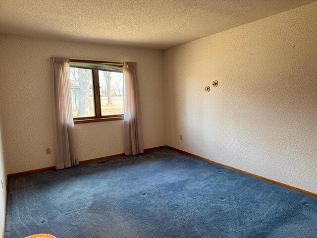 carpeted empty room featuring visible vents, a textured ceiling, and wallpapered walls