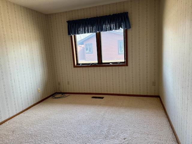 spare room featuring baseboards, carpet flooring, visible vents, and wallpapered walls