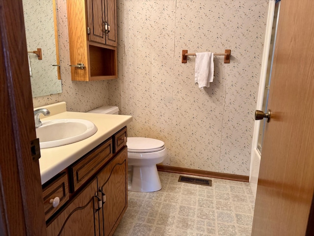 bathroom with toilet, visible vents, baseboards, vanity, and wallpapered walls