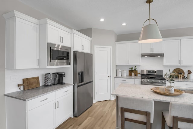 kitchen with a breakfast bar area, stainless steel appliances, backsplash, white cabinetry, and under cabinet range hood