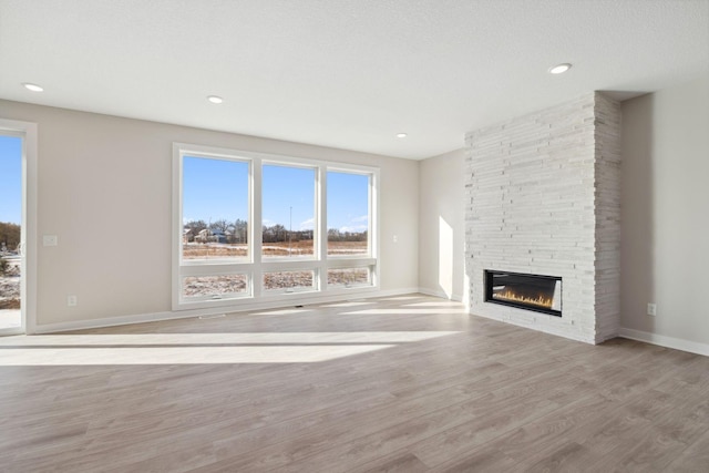 unfurnished living room with a textured ceiling, a stone fireplace, recessed lighting, wood finished floors, and baseboards