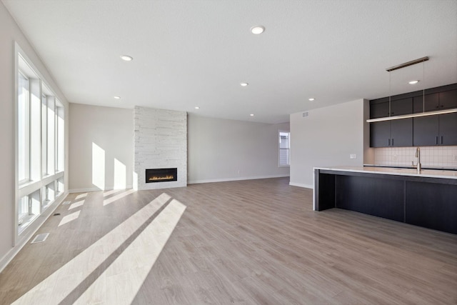 unfurnished living room featuring recessed lighting, a fireplace, visible vents, baseboards, and light wood-type flooring