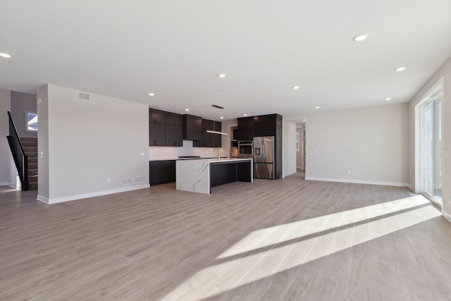 kitchen featuring a kitchen island with sink, open floor plan, light countertops, appliances with stainless steel finishes, and modern cabinets