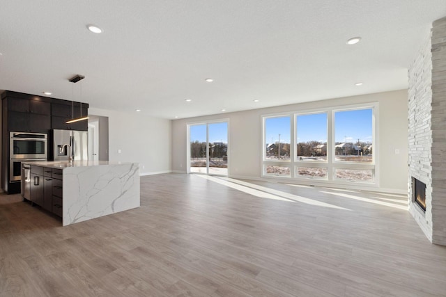 kitchen featuring an island with sink, modern cabinets, light stone countertops, light wood-type flooring, and a fireplace