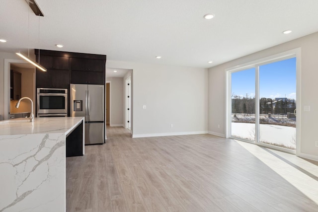 kitchen featuring modern cabinets, stainless steel appliances, light wood-style floors, pendant lighting, and a sink