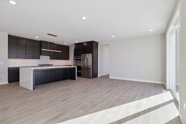 kitchen featuring light countertops, light wood-style flooring, appliances with stainless steel finishes, a kitchen island with sink, and modern cabinets