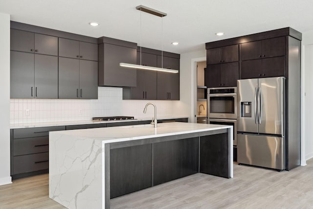 kitchen featuring appliances with stainless steel finishes, a sink, light wood-style flooring, and decorative backsplash