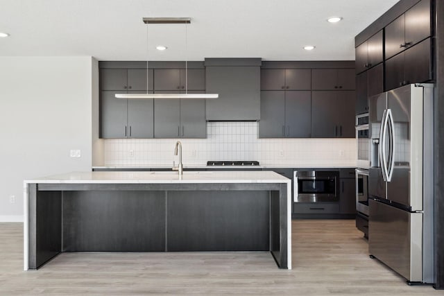 kitchen with light wood-style flooring, a sink, stainless steel appliances, pendant lighting, and backsplash