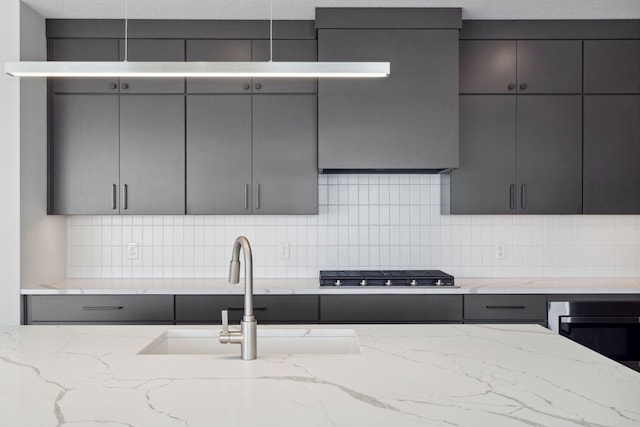 kitchen with stainless steel gas cooktop, decorative backsplash, gray cabinetry, a sink, and light stone countertops