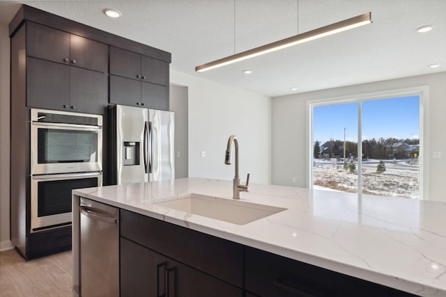 kitchen with light wood-style flooring, appliances with stainless steel finishes, a sink, a textured ceiling, and light stone countertops