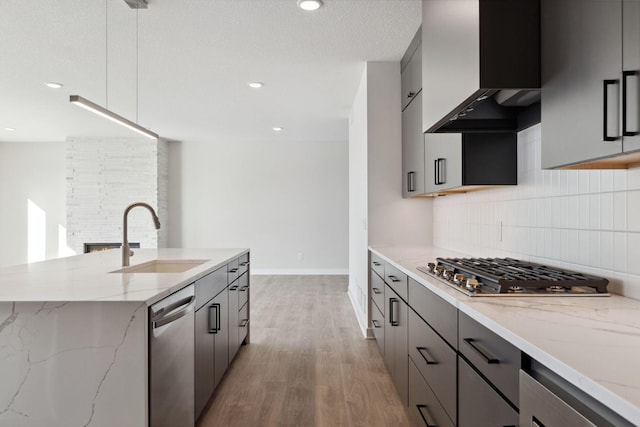 kitchen with light stone counters, decorative backsplash, appliances with stainless steel finishes, a sink, and wall chimney exhaust hood