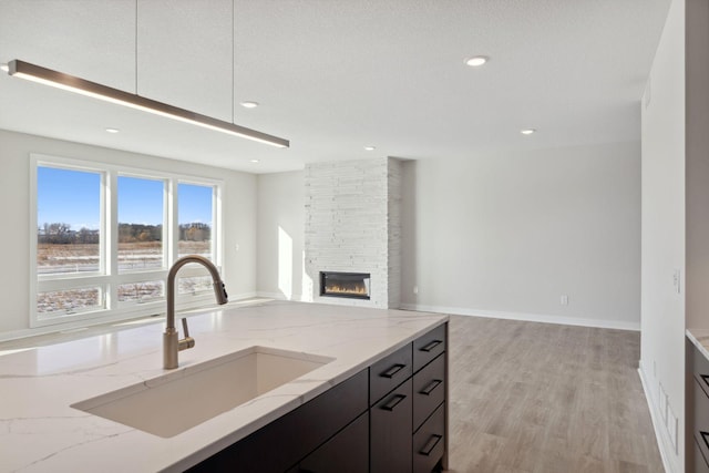 kitchen featuring light stone counters, light wood-style floors, a sink, a stone fireplace, and modern cabinets