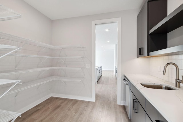 interior space featuring tasteful backsplash, light stone countertops, light wood-type flooring, open shelves, and a sink