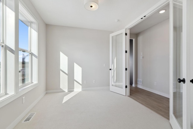 carpeted empty room with french doors, plenty of natural light, visible vents, and baseboards