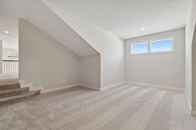 additional living space with a textured ceiling, recessed lighting, light colored carpet, baseboards, and vaulted ceiling