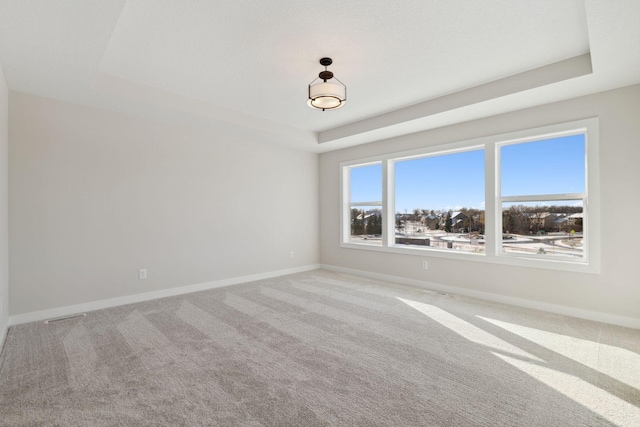 unfurnished room with a tray ceiling, carpet flooring, visible vents, and baseboards